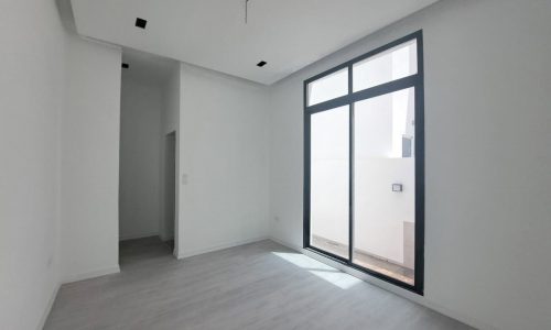 Empty modern villa for sale with white walls, gray flooring, and large glass door letting natural light in, located in a peaceful area.