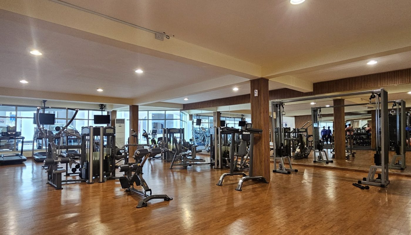 A spacious gym with wooden flooring, various exercise machines, and large mirrors on the walls.