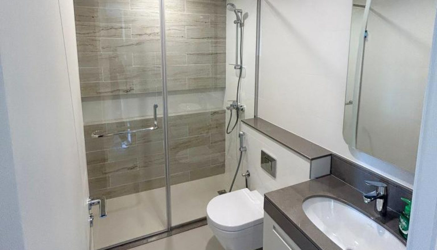 Modern bathroom with a glass-enclosed shower, wall-mounted toilet, large mirror, and a sink with a gray countertop and storage drawers below.