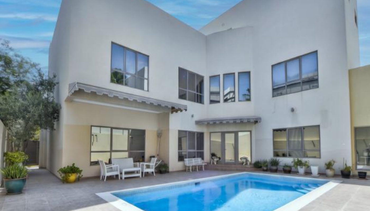 Modern two-story white house with large windows, a tiled patio, and a rectangular swimming pool surrounded by potted plants under a blue sky.