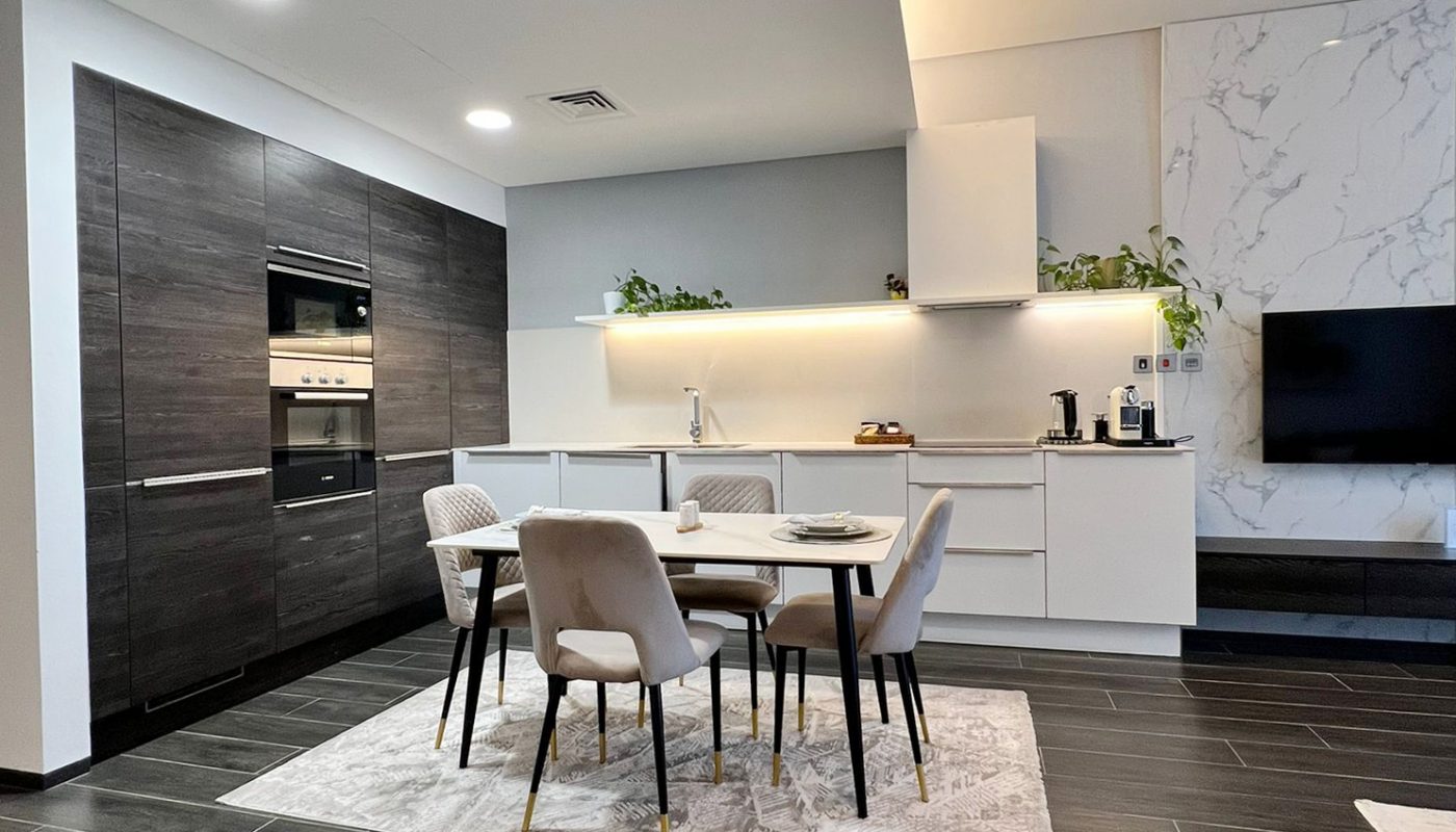 Modern open-plan kitchen and dining area with dark wood cabinets, white countertops, a dining table with four chairs, tile flooring, and minimal décor.