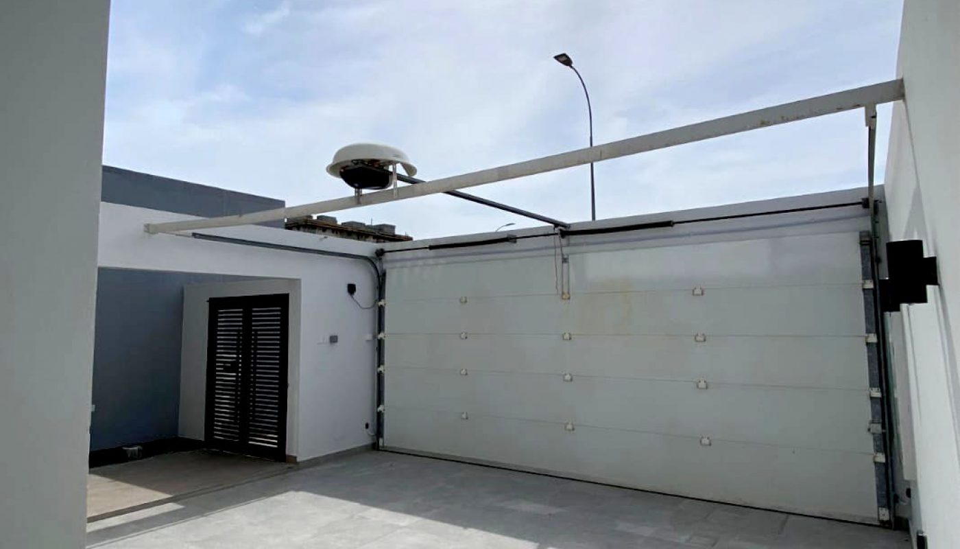 A modern, empty garage with a closed white sectional door, tiled floor, and sunlight streaming in through an open roof.