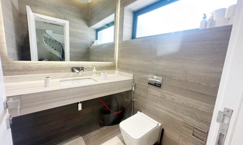 A modern villa in Hamala featuring a bathroom with a toilet, sink, and mirror.