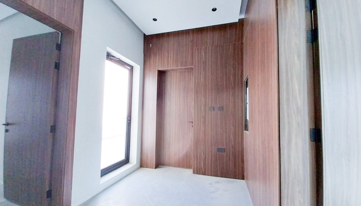 A modern, empty room with wooden wall paneling, a large window, and two doors, one open and one closed. The floor is light-colored tile.