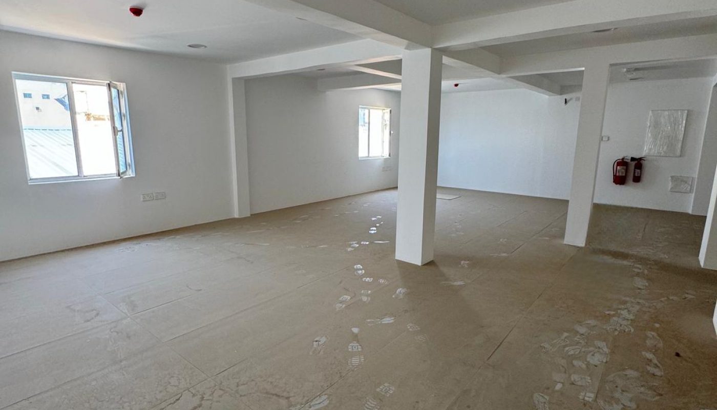An empty, unfurnished room with white walls, large windows, and columns; the floor is covered with protective material and visible footprints.