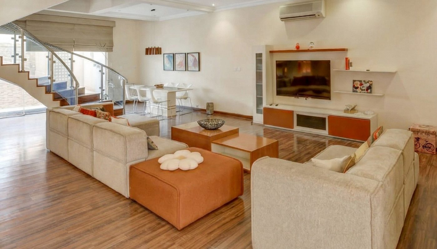 Spacious modern living room with beige sofas, wooden flooring, a TV unit, and an open staircase leading to an upper floor.