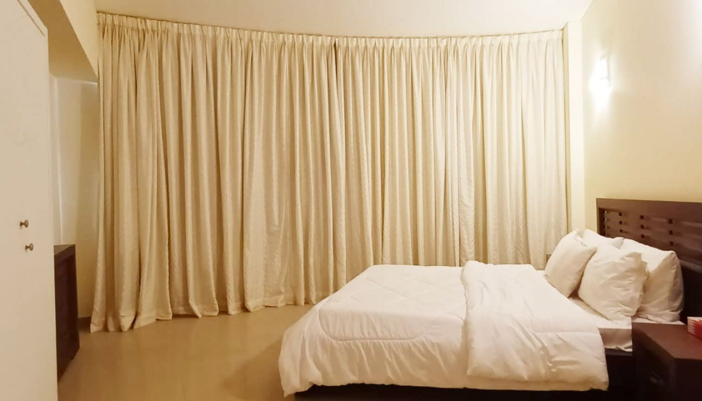 A modern bedroom with a white bed and white curtains in an apartment.