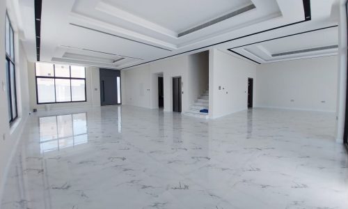 Spacious, empty room with marble-patterned tile flooring, white walls, large windows, and a staircase in the background.