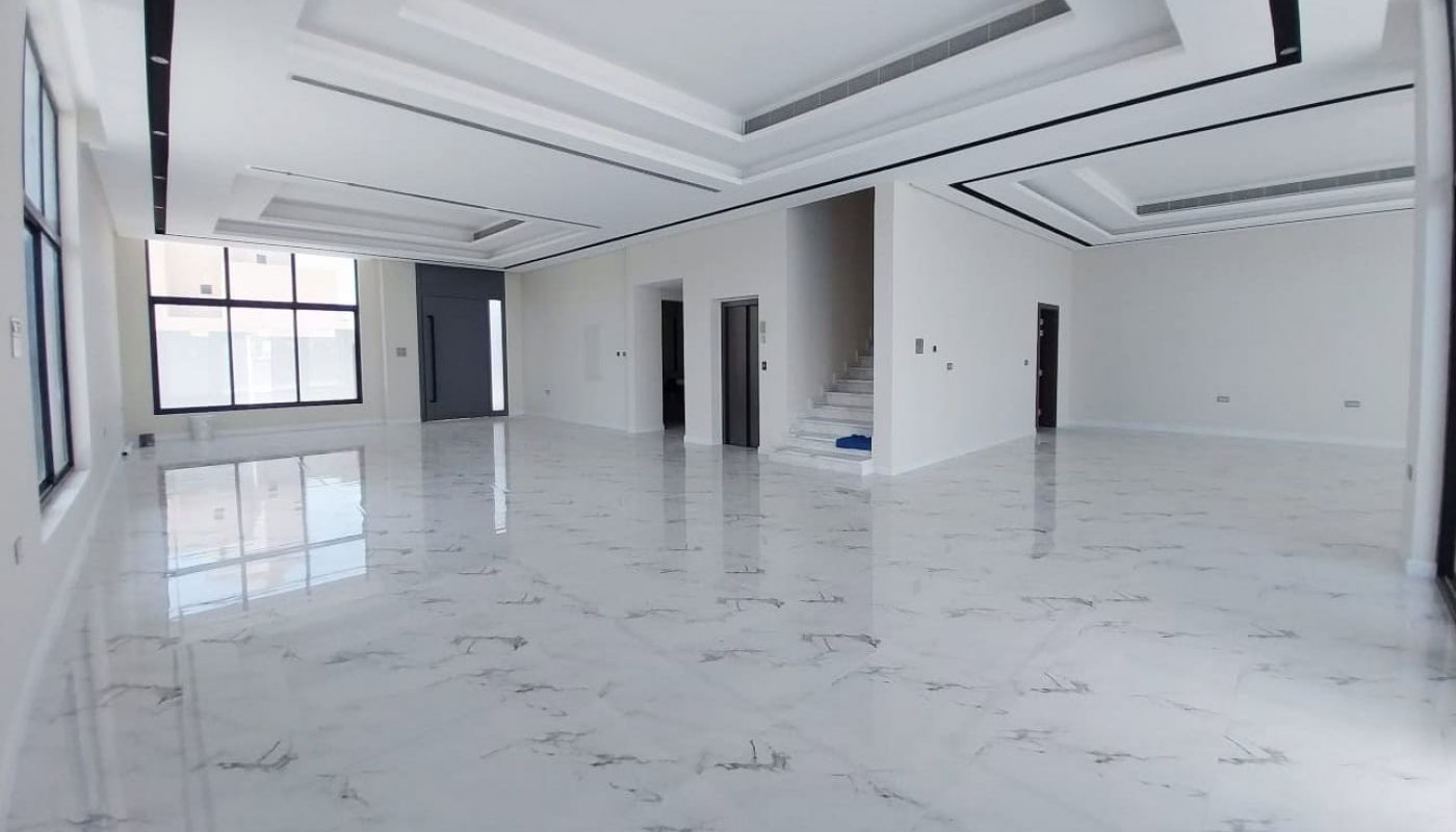 Spacious, empty room with white marble floors, large windows, white walls, recessed ceiling, and a staircase leading to an upper floor.