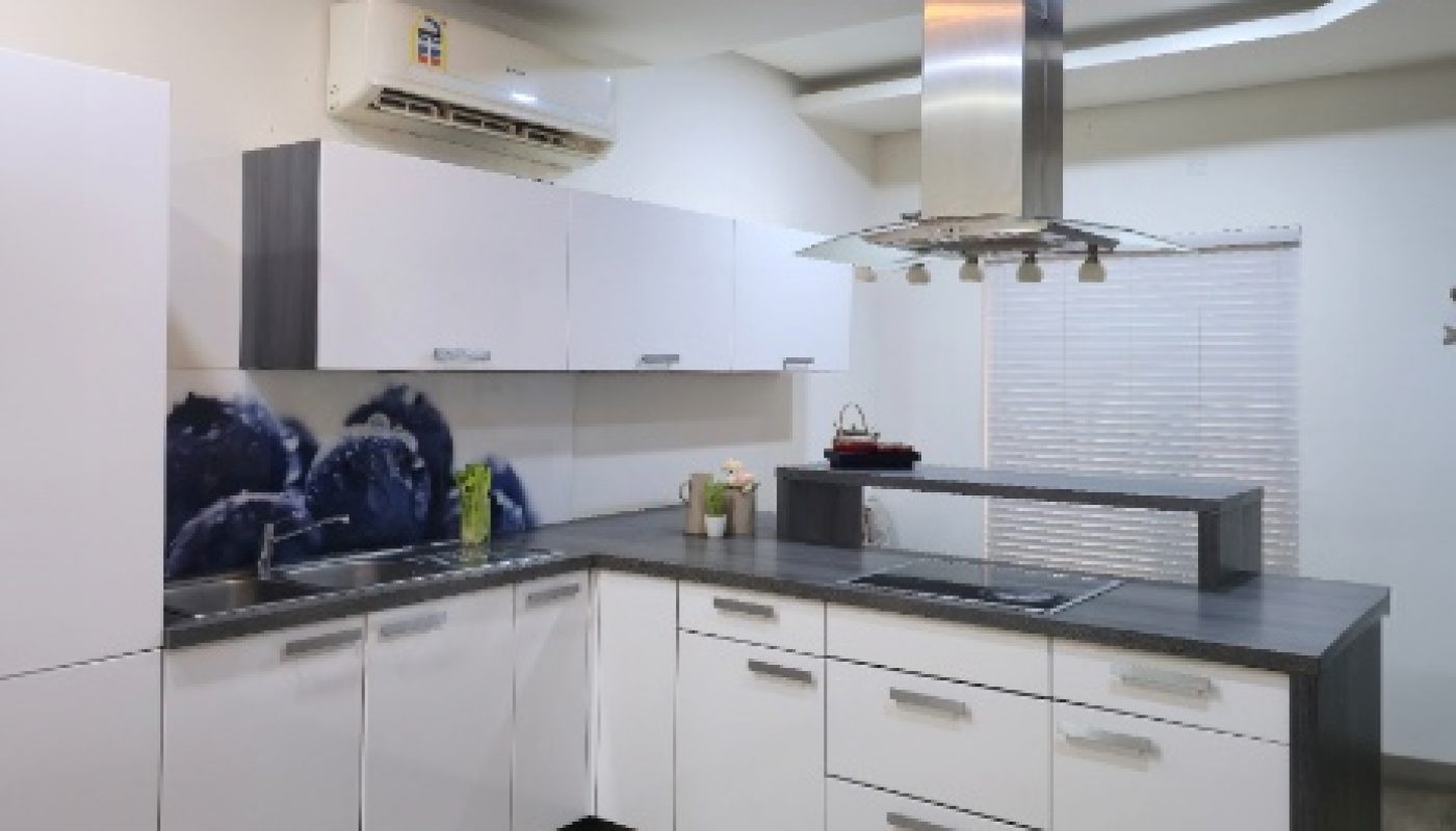 Modern kitchen with white cabinets, grey countertops, stainless steel range hood, air conditioner, and wooden floor. A dining table is partially visible in the foreground.