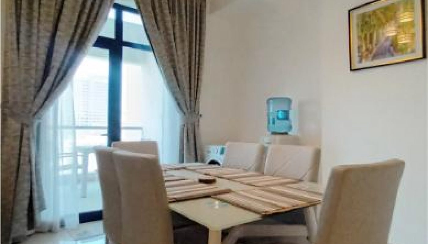 A modern dining area with a glass table set for four, beige chairs, large window with curtains, wall art, and a water dispenser in the corner.