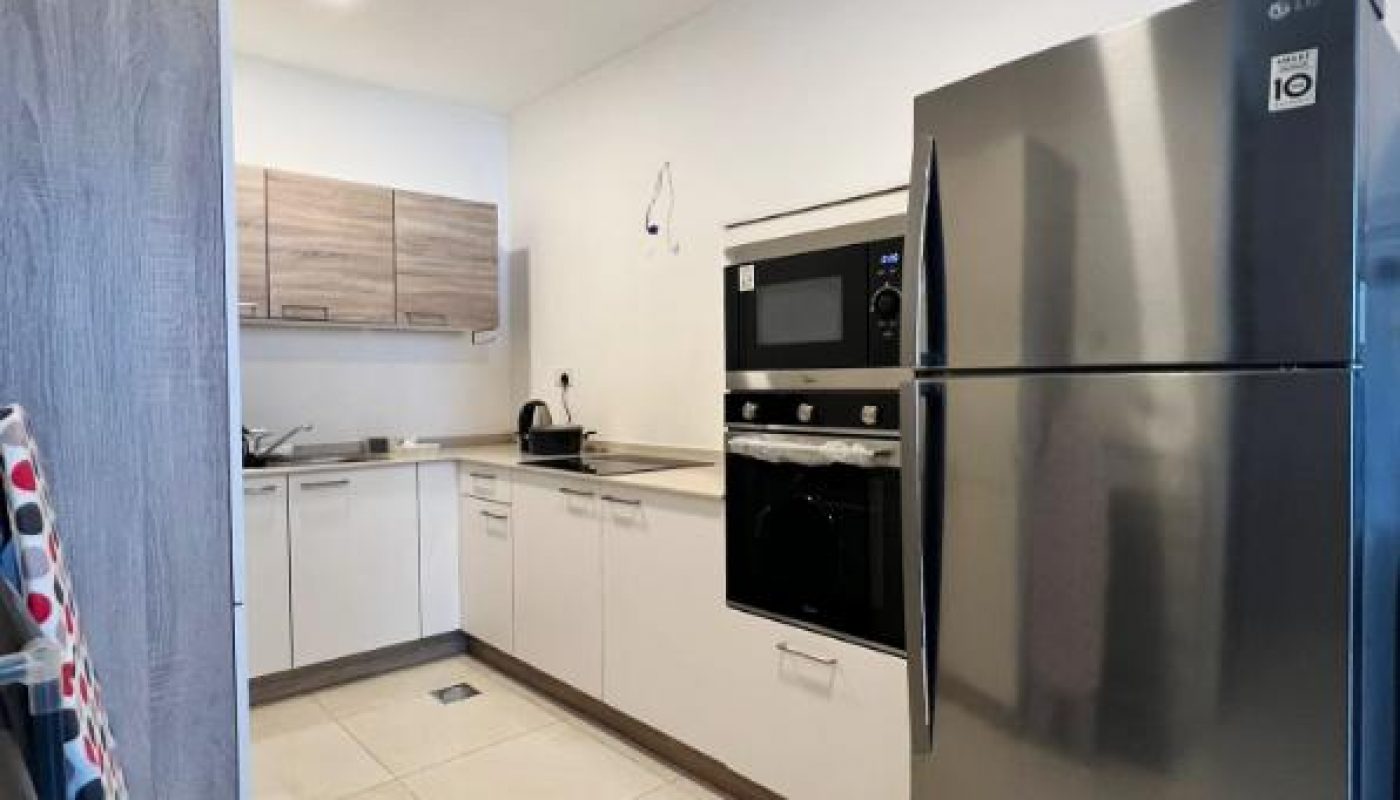 Modern kitchen with white cabinets, stainless steel refrigerator, built-in oven and microwave, and wooden overhead cupboards. Countertop has a kettle and a few small items.