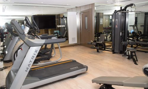 A fully furnished gym room with a treadmill, elliptical, and weights.