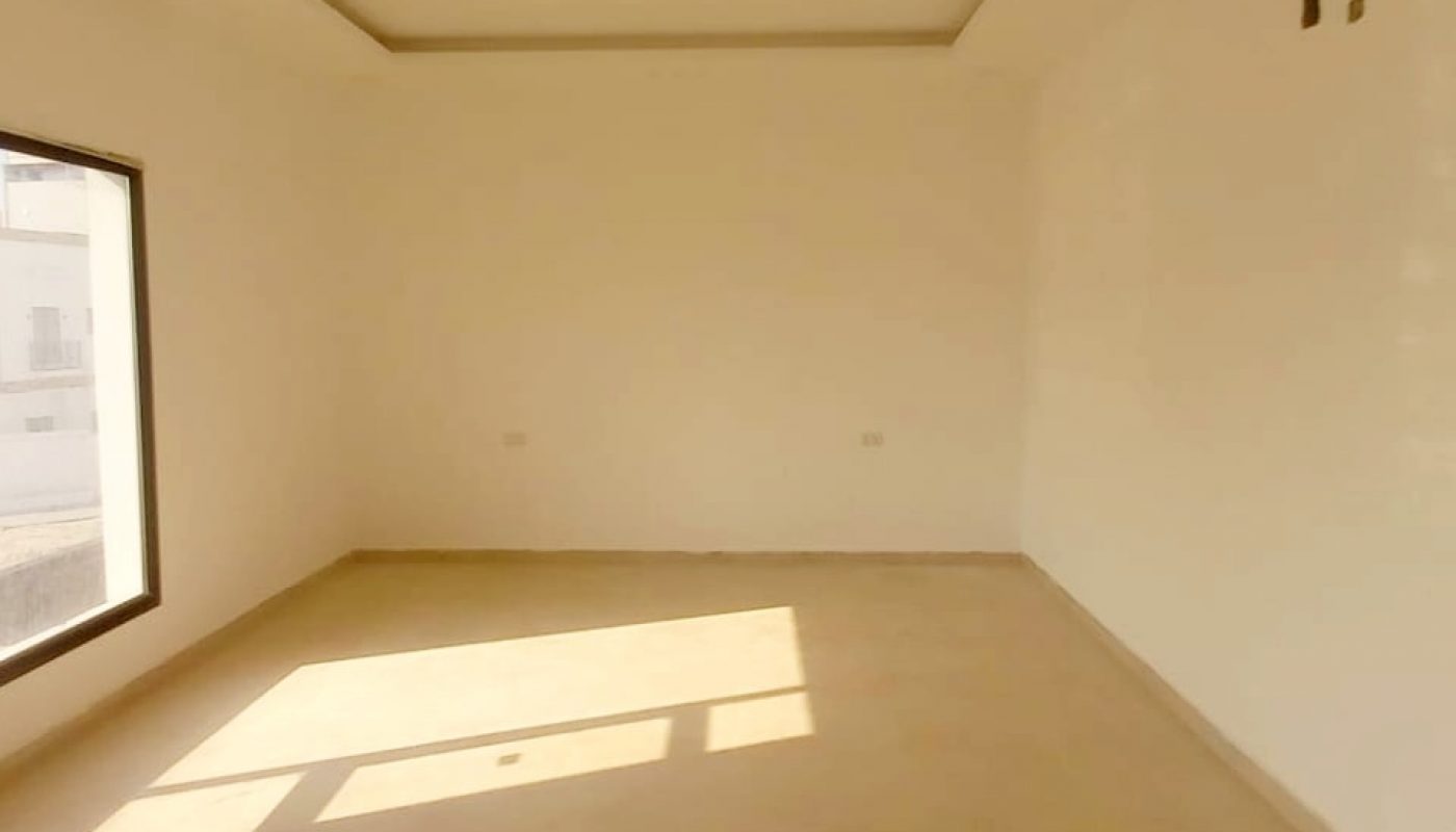 A sale villa in Bani Jamra with spacious empty rooms, white walls, and a window offering natural light.