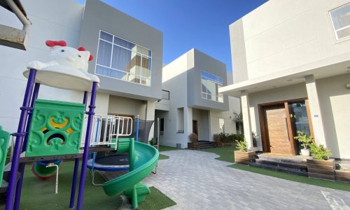 A children's play area in front of three villas in a residential compound located in Al Janabiyah.