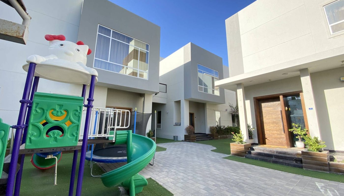 A children's play area in front of three villas in a residential compound located in Al Janabiyah.