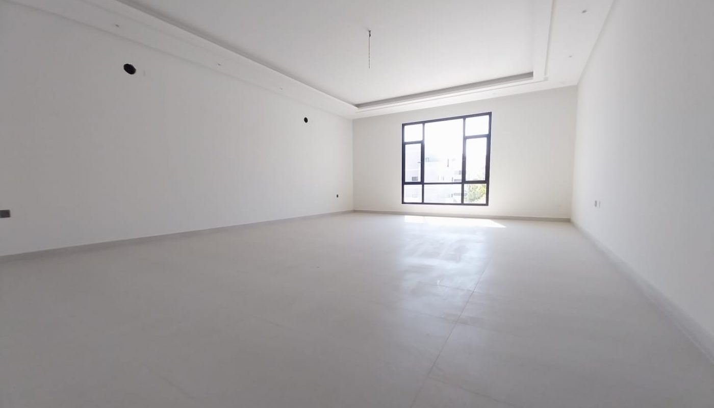 Empty, spacious room with white walls, tiled floor, large window letting in natural light, and ceiling light fixture.