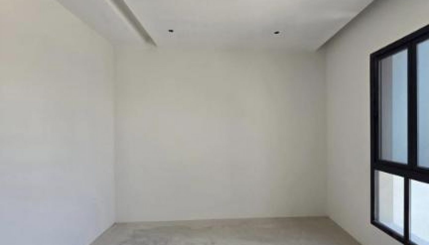 Empty, unfurnished room with white walls, a ceiling with recessed lights, a large window on the right wall, and a bare floor.