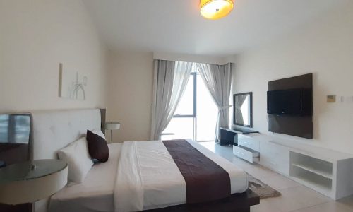 Fully furnished bedroom with a large bed and TV in an apartment for rent in Al Mahooz.