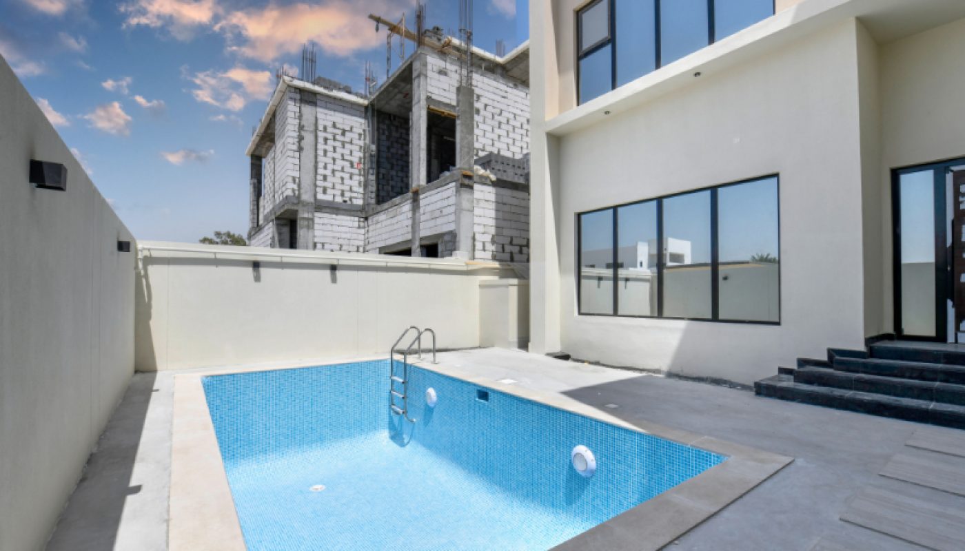Unfilled swimming pool in a modern residential courtyard, with a ladder and steps, adjacent to a building under construction in the background.