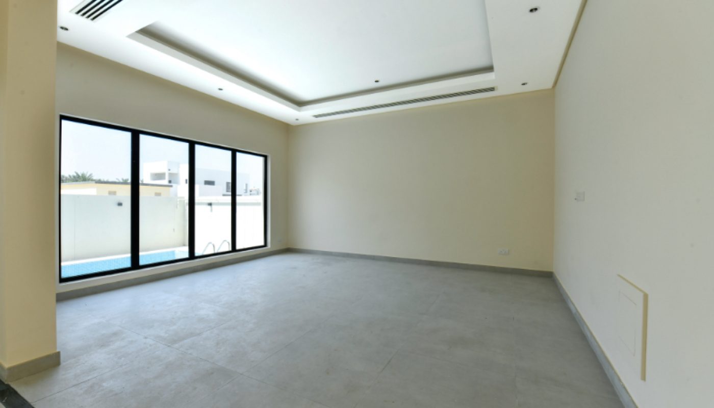 Empty modern room with large windows, light-colored walls, tiled floor, recessed ceiling lighting, and a view of a pool outside.