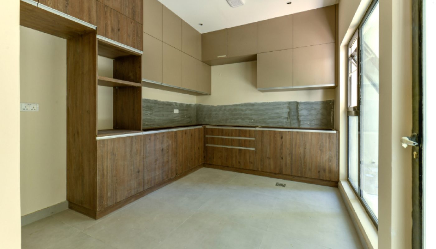 Modern kitchen with wood and beige cabinetry, grey tile backsplash, large window on the right, and no appliances or furniture present.