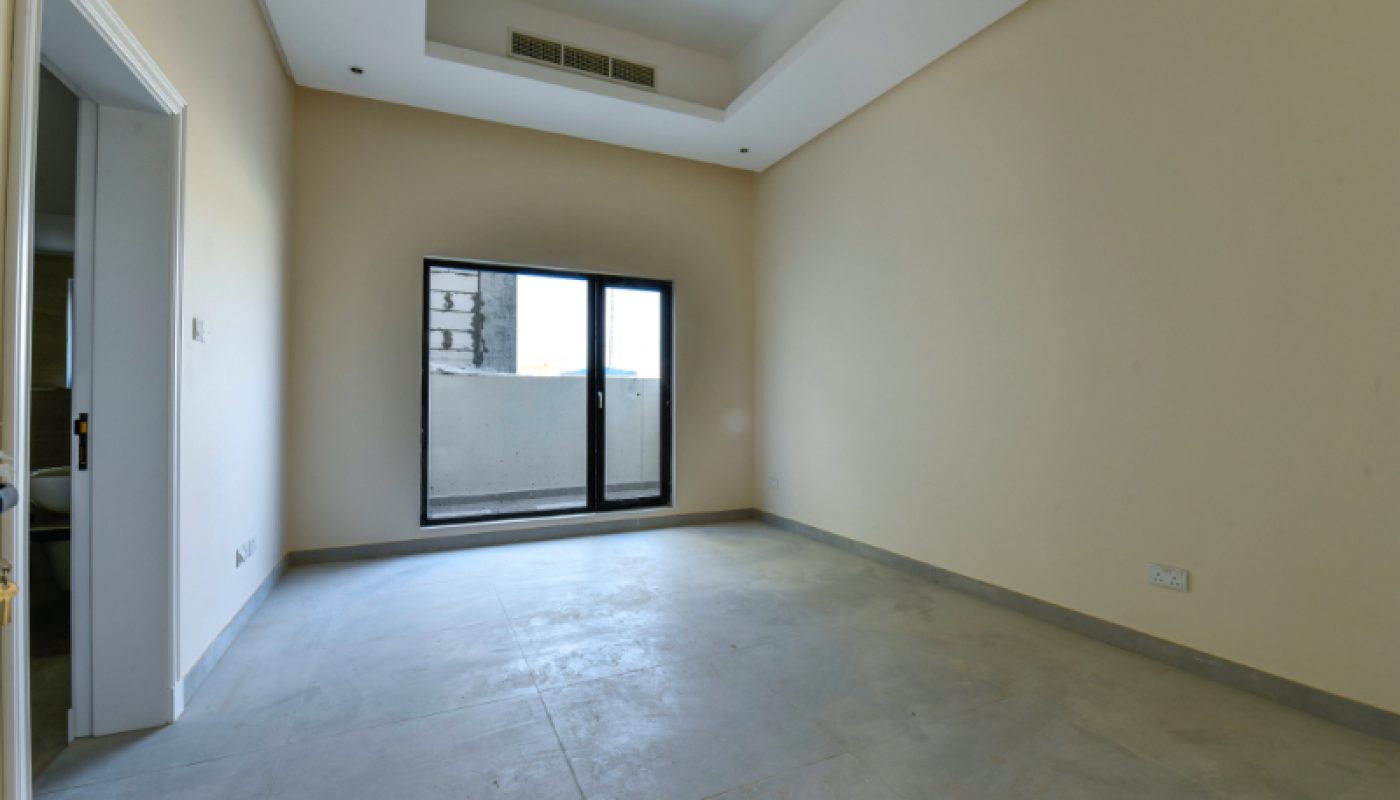 Empty room with beige walls, gray tiled floor, a ceiling vent, and a glass door leading to a small balcony or outdoor area.