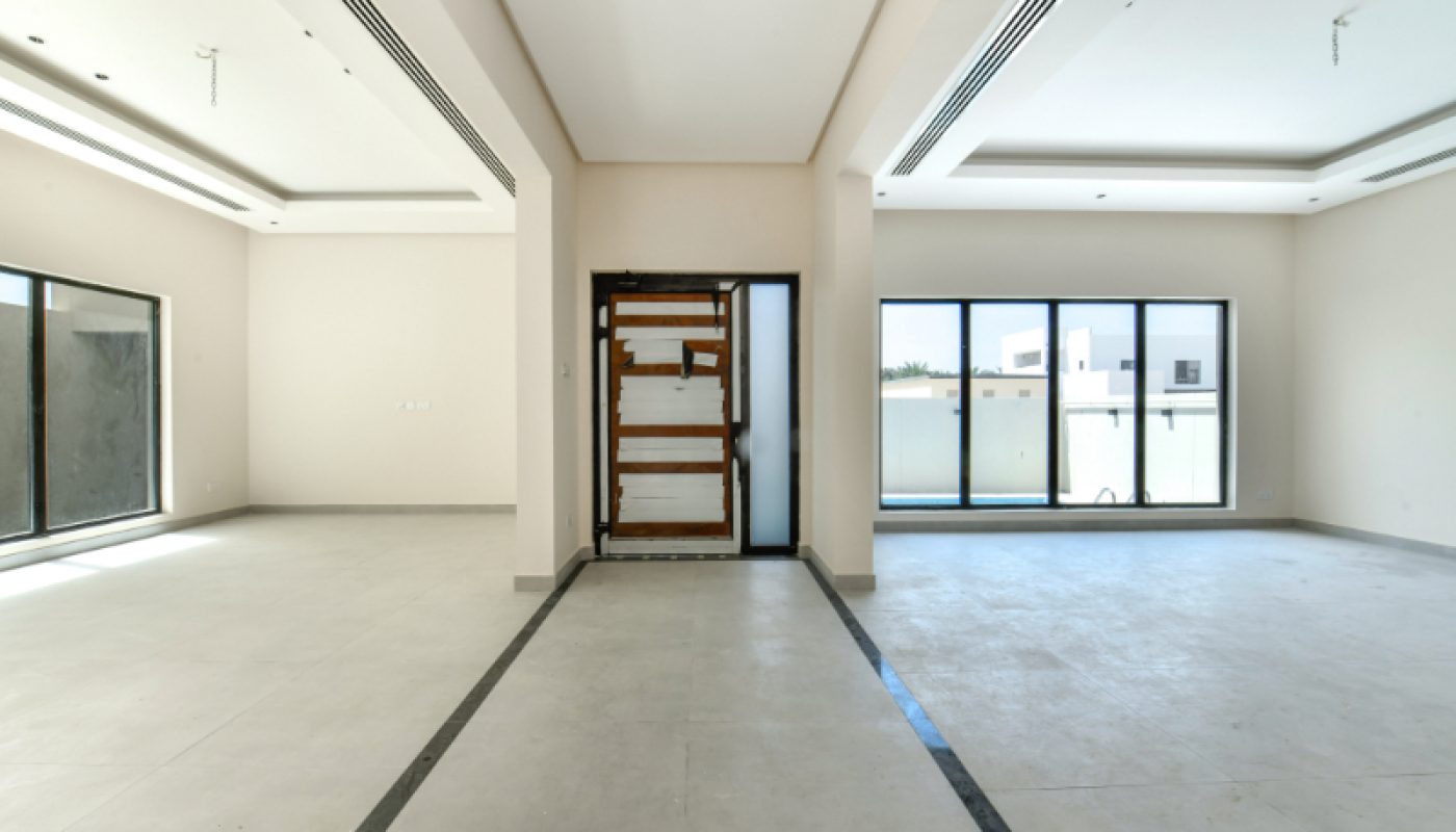 Unfurnished, modern empty room with large windows, white walls, tiled floor, and a front door covered with wooden boards.