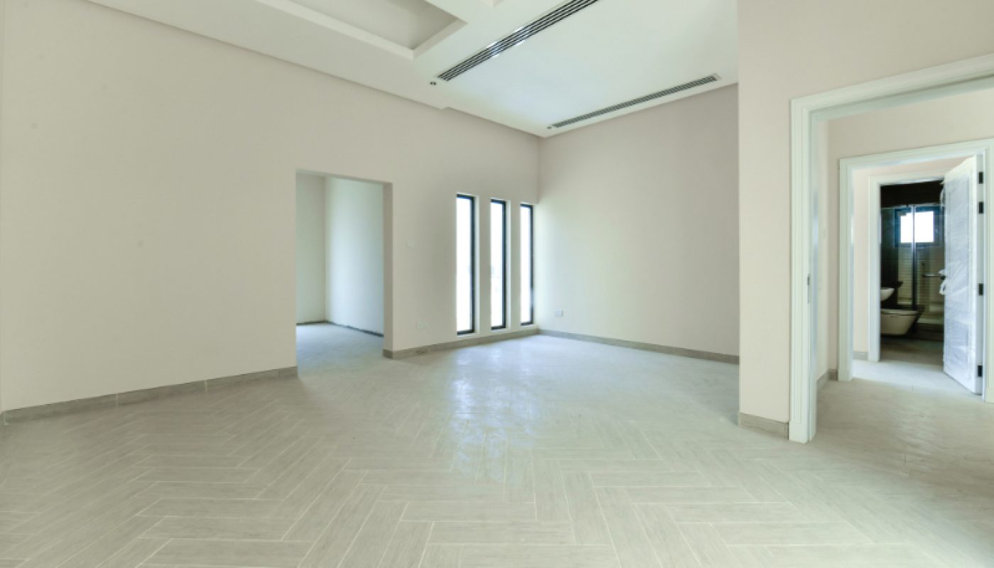 Spacious empty room with light-colored tile flooring, large windows, white walls, and open doorways leading to adjacent rooms and a bathroom.