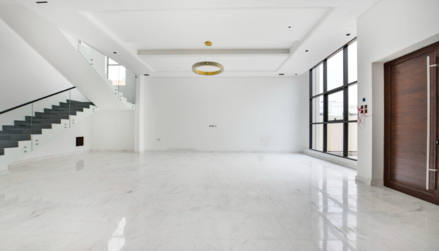 Spacious, empty, modern living room with white marble floor, staircase, large windows, a wooden door, and a ceiling light fixture.