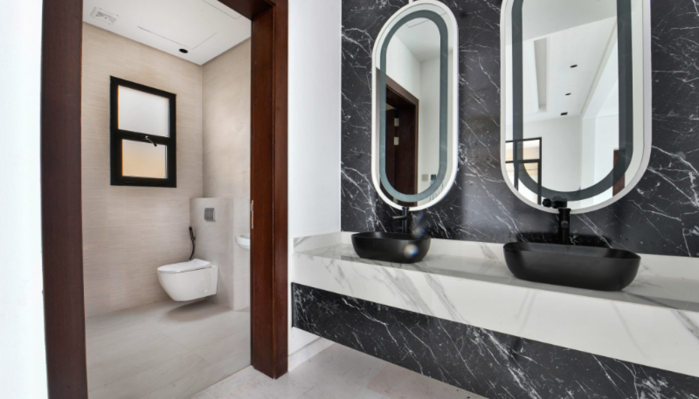 Modern bathroom with a double sink vanity featuring black basins and oval mirrors, and a separate toilet area with a wall-mounted toilet.