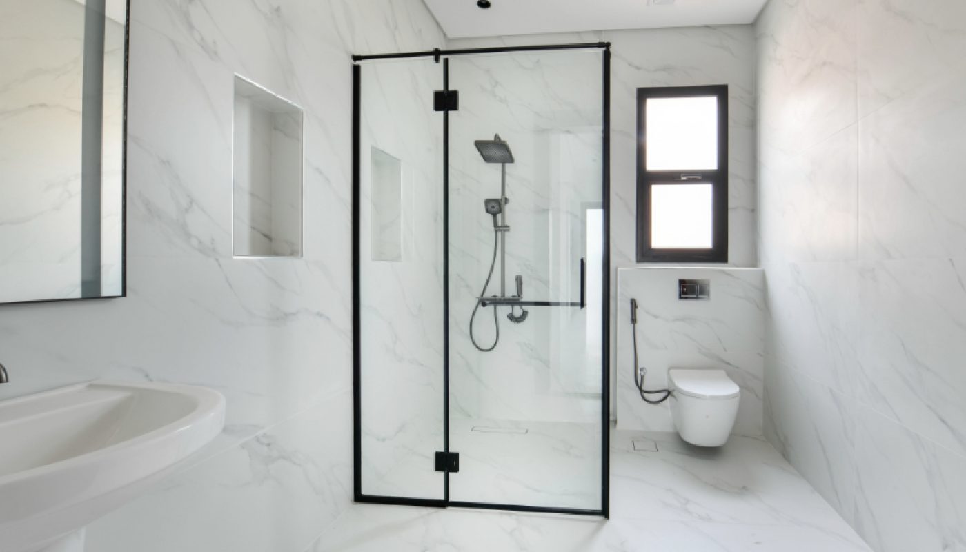Modern bathroom with white marble walls, a glass shower enclosure with black trim, a wall-mounted toilet, and a window.