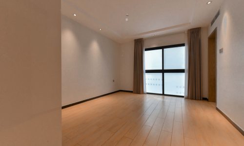 An empty room with stunning wooden floors near a sliding glass door.