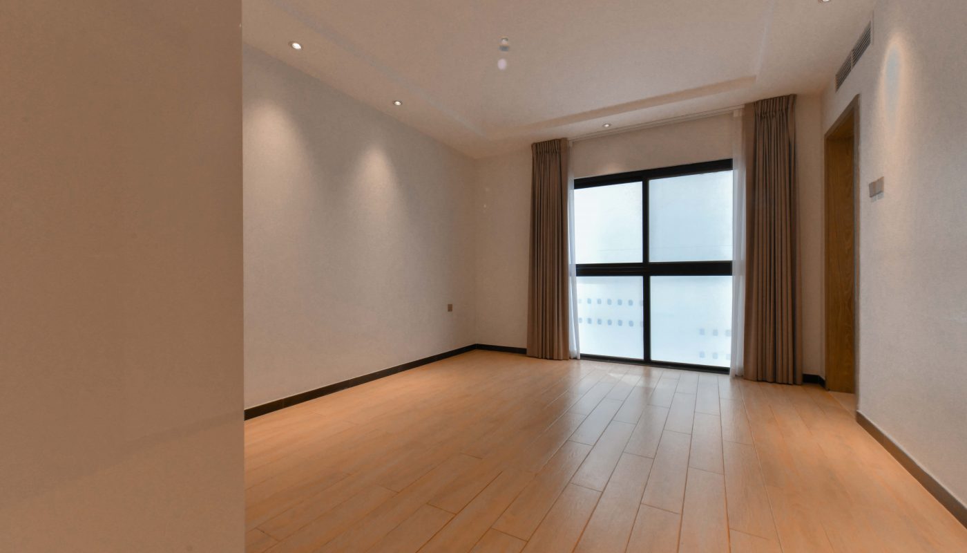 An empty room with stunning wooden floors near a sliding glass door.
