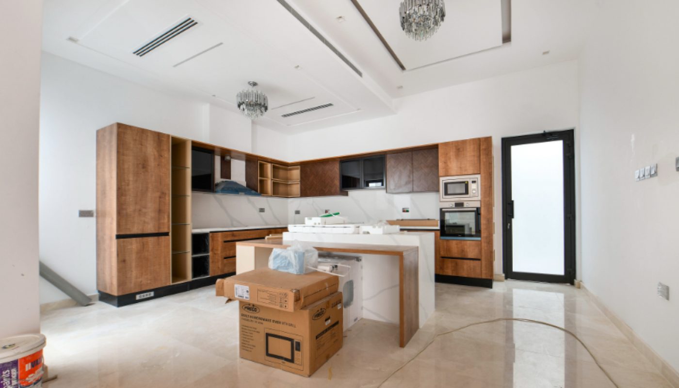 Modern kitchen with wooden cabinets, white countertops, and two pendant lights; cardboard boxes and supplies are scattered, suggesting recent renovations or moving in.