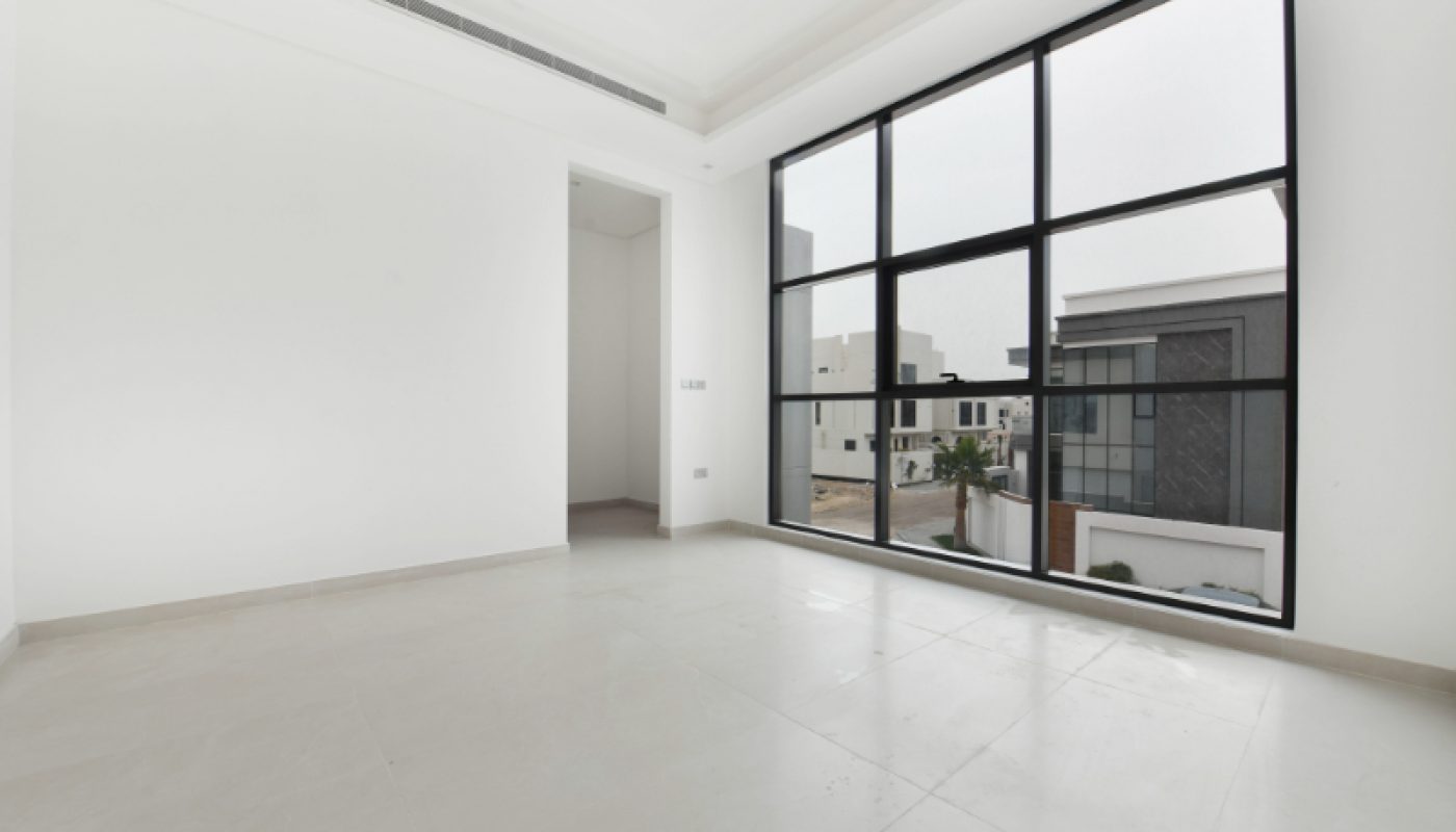 Empty, modern room with large floor-to-ceiling windows, white walls, beige tiled floor, and a view of neighboring buildings outside.