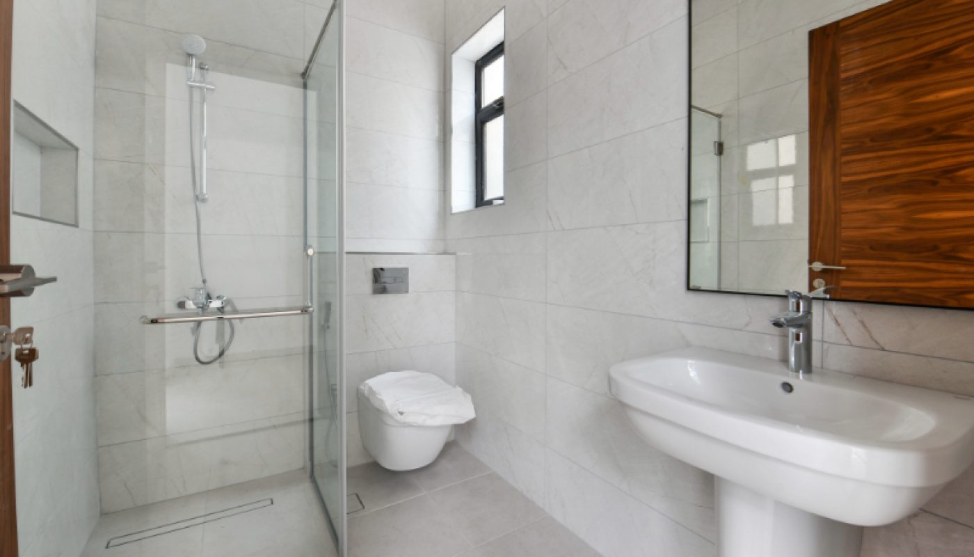 Modern bathroom with white tiled walls, a glass-enclosed shower, wall-mounted toilet, rectangular sink, large mirror, and a wooden door.