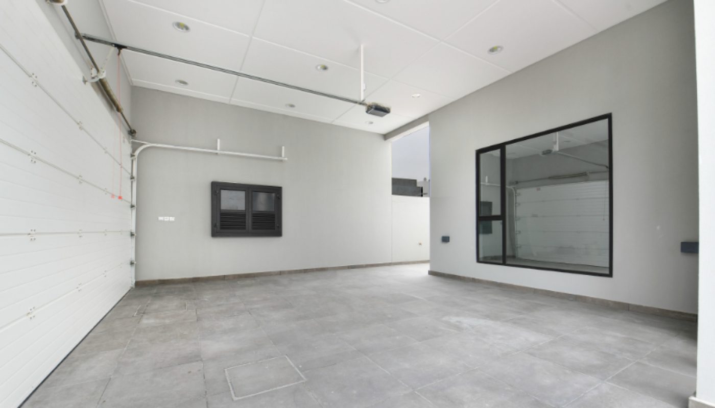 Modern, empty garage with gray tiled floor, white ceiling, large window, and a closed sectional garage door.