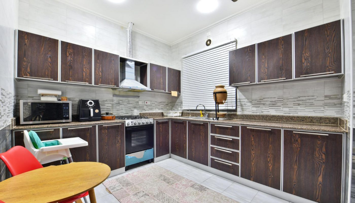 Modern kitchen with dark wood cabinets, granite countertops, stainless steel appliances, a round table with red chairs, and a window with blinds.