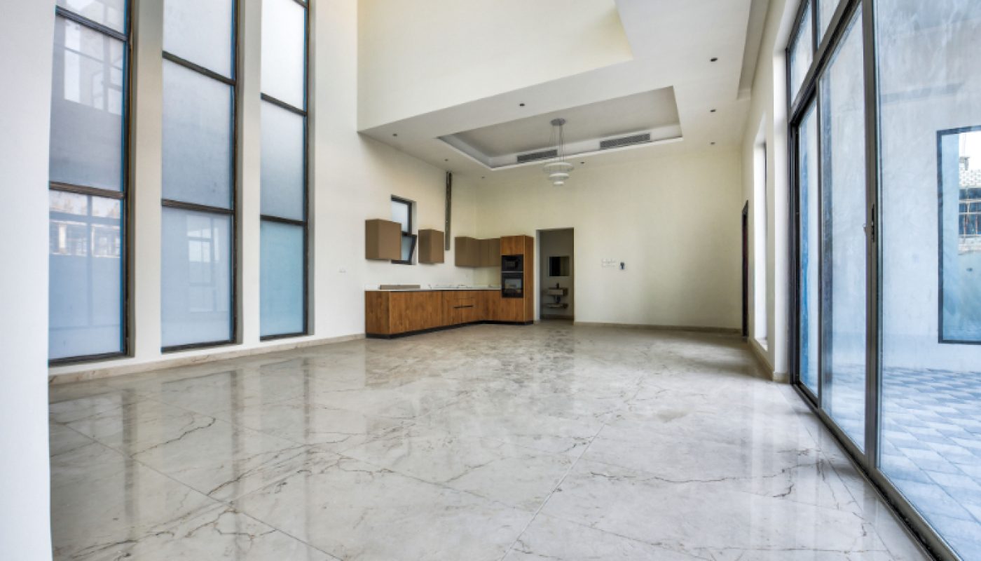 Spacious, modern empty room with marble floors, high ceilings, large windows, and a minimalist kitchen area in the back.