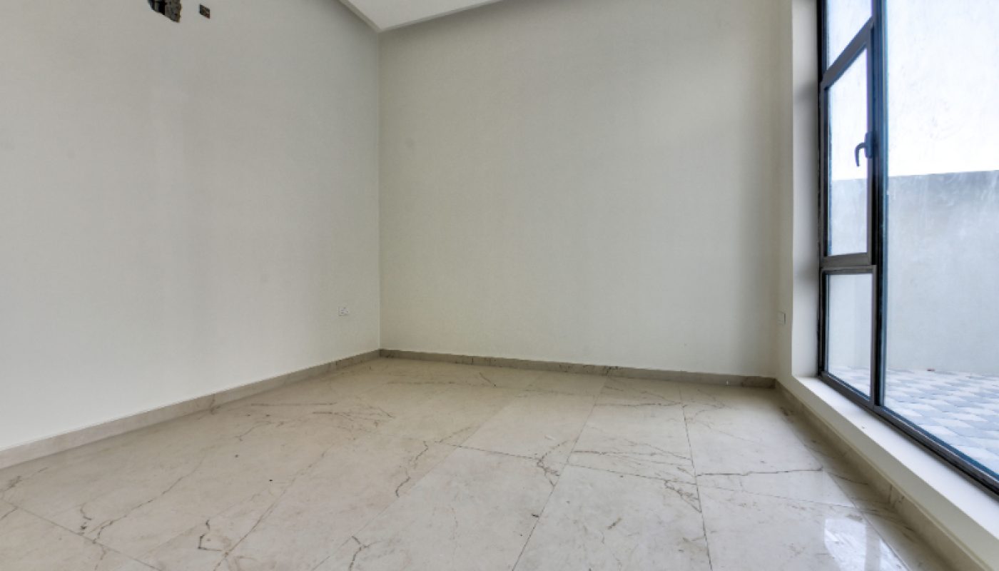 Empty room with off-white walls, marble tile flooring, and a large window allowing natural light; visible outdoor area through the window.