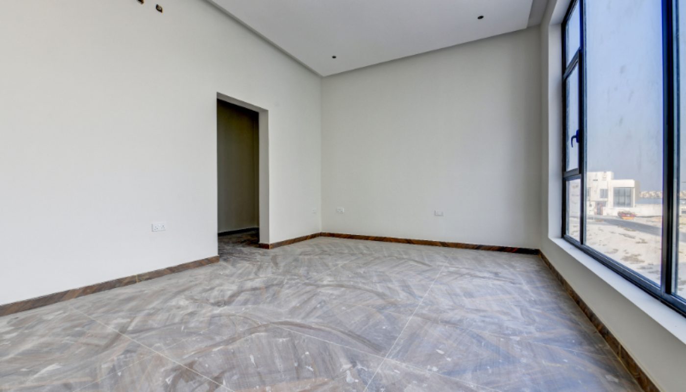 Empty, unfurnished room with white walls, marble tile flooring, recessed ceiling lights, a doorway, and large windows letting in natural light.