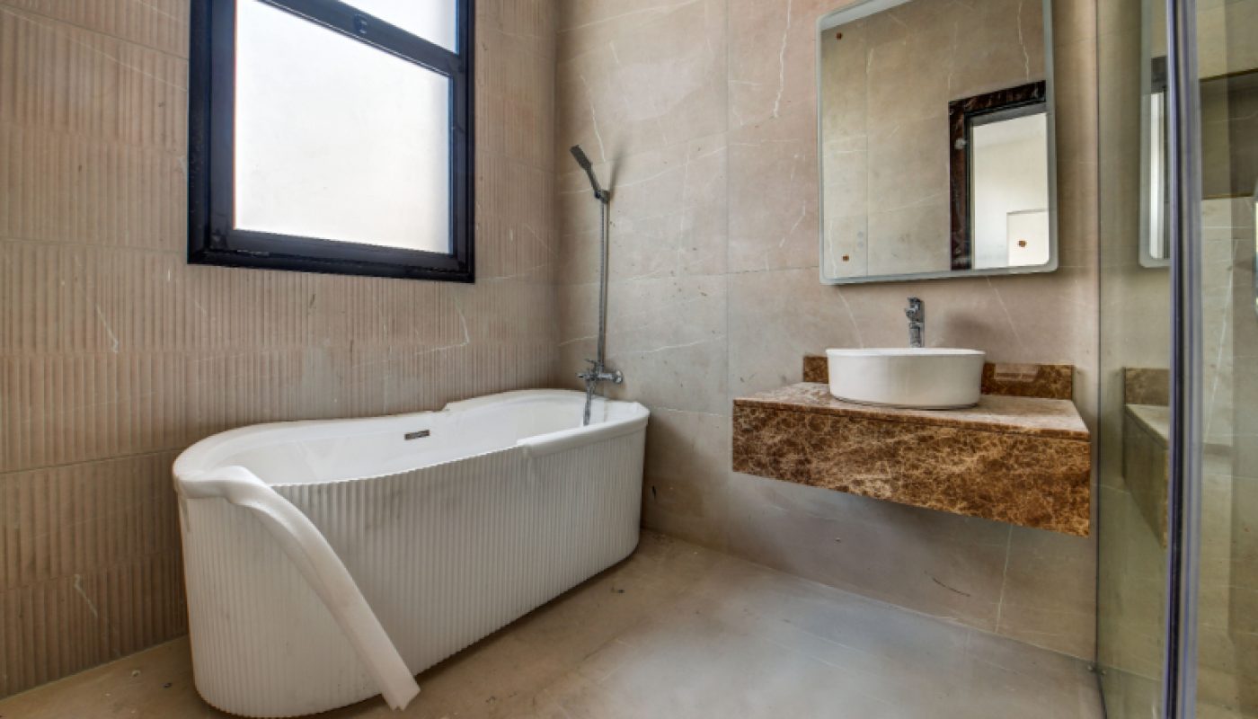 Modern bathroom with a white bathtub, wall-mounted sink with a brown marble countertop, rectangular mirror, and a frosted window.