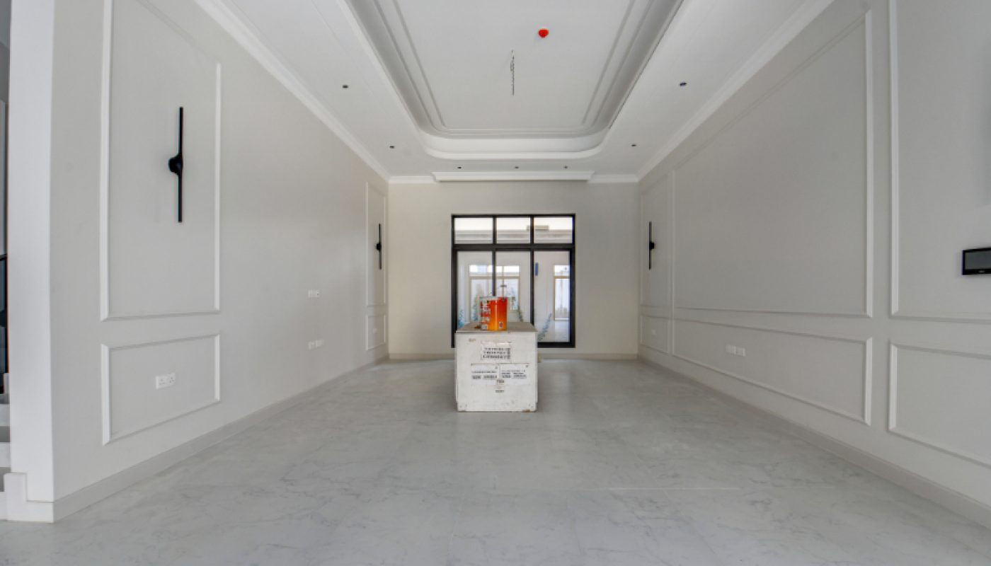 Empty modern room with white walls, minimal ceiling details, large windows at the far end, and a single box placed in the center of the floor.