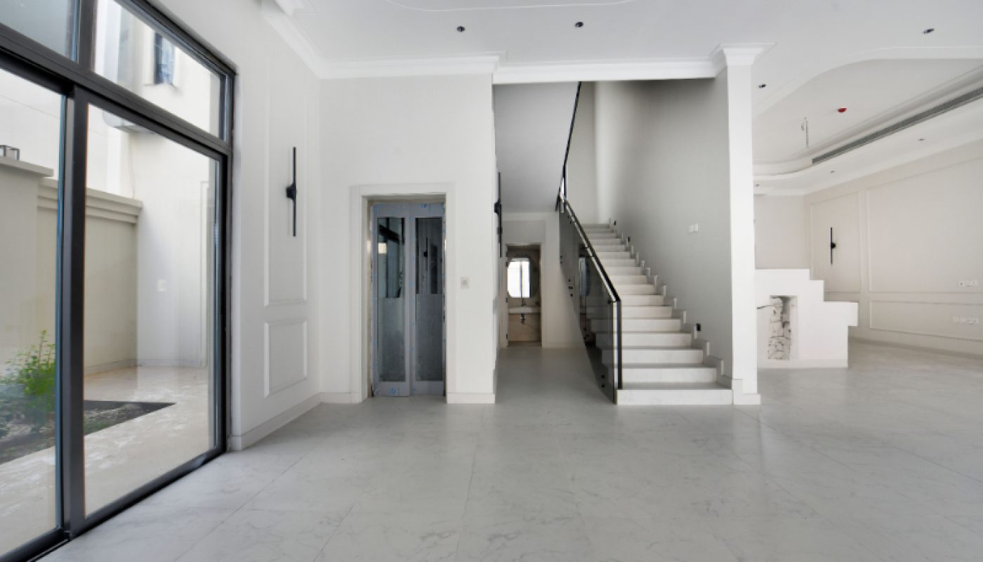 Modern, spacious interior with white marble floors, a staircase with a black railing, an elevator, large windows, and minimalistic decor.