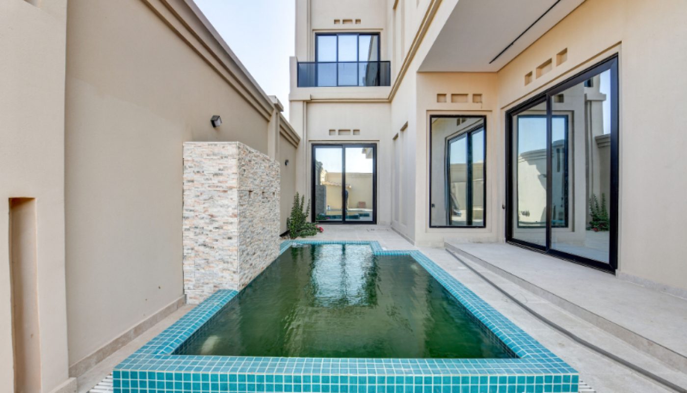 A small rectangular pool with turquoise tiles is surrounded by beige walls and glass doors in a modern courtyard.