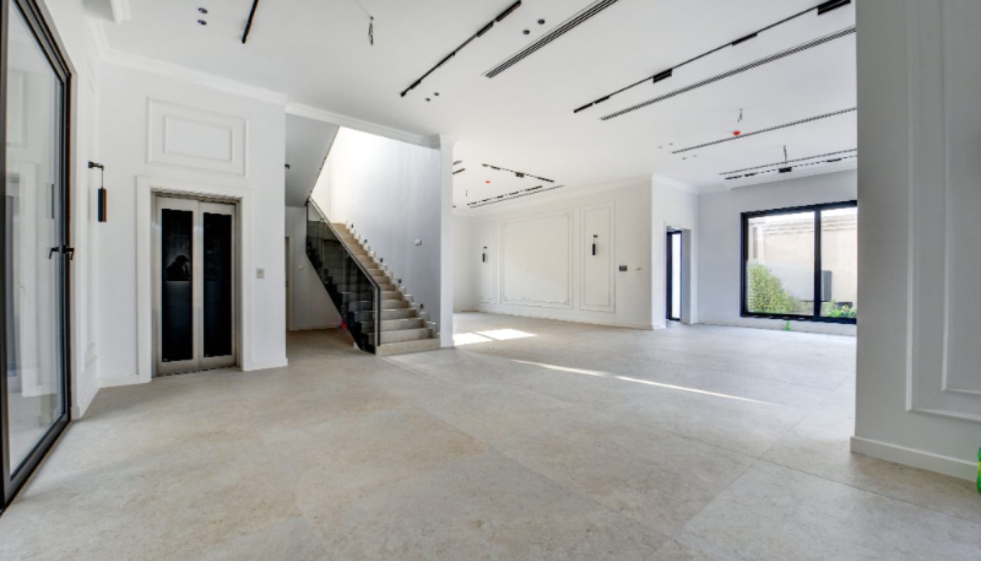 Spacious, empty modern interior with large tiled floor, staircase, elevator, and floor-to-ceiling windows allowing natural light.