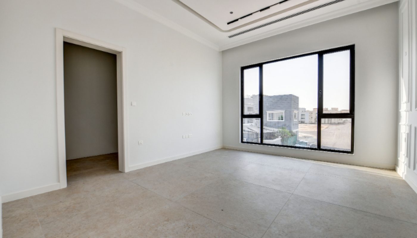 Empty, unfurnished room with large window, tiled floor, white walls, and an open doorway leading to another area. Daylight enters through the window.