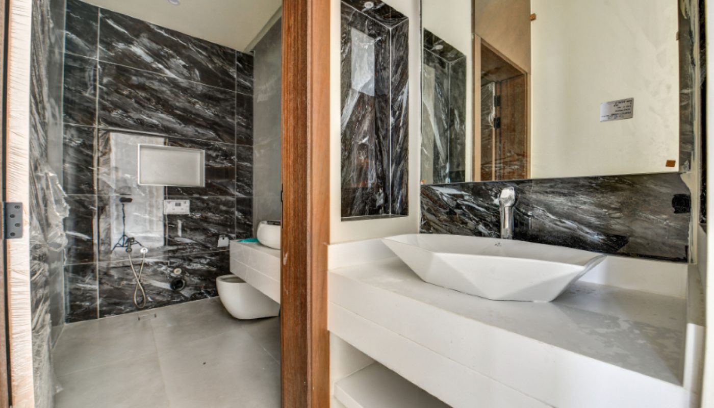 Modern bathroom with black marble wall tiles, a white toilet, bidet, and a white sink on a countertop with a large mirror above.