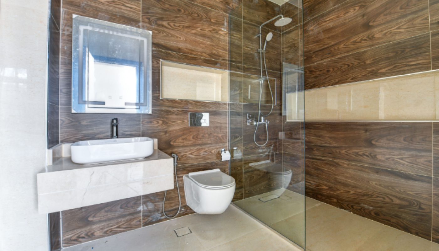 Modern bathroom with wood-patterned walls, a floating sink, wall-mounted toilet, and a glass-enclosed shower area.